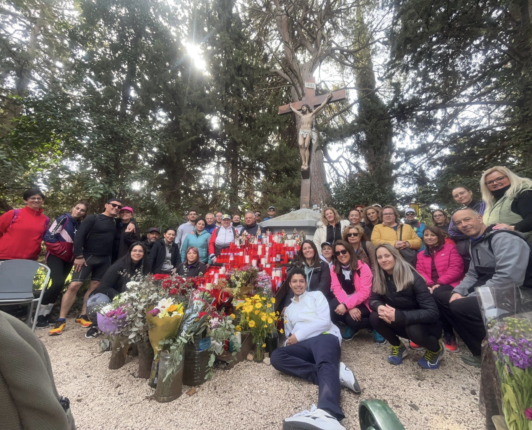 Grupo de socios en una salida al campo, con flores y velas junto a una cruz