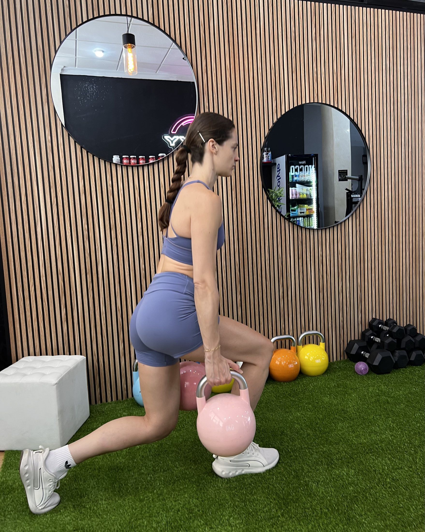 Zancada con kettlebell sobre el césped, junto a los espejos redondos