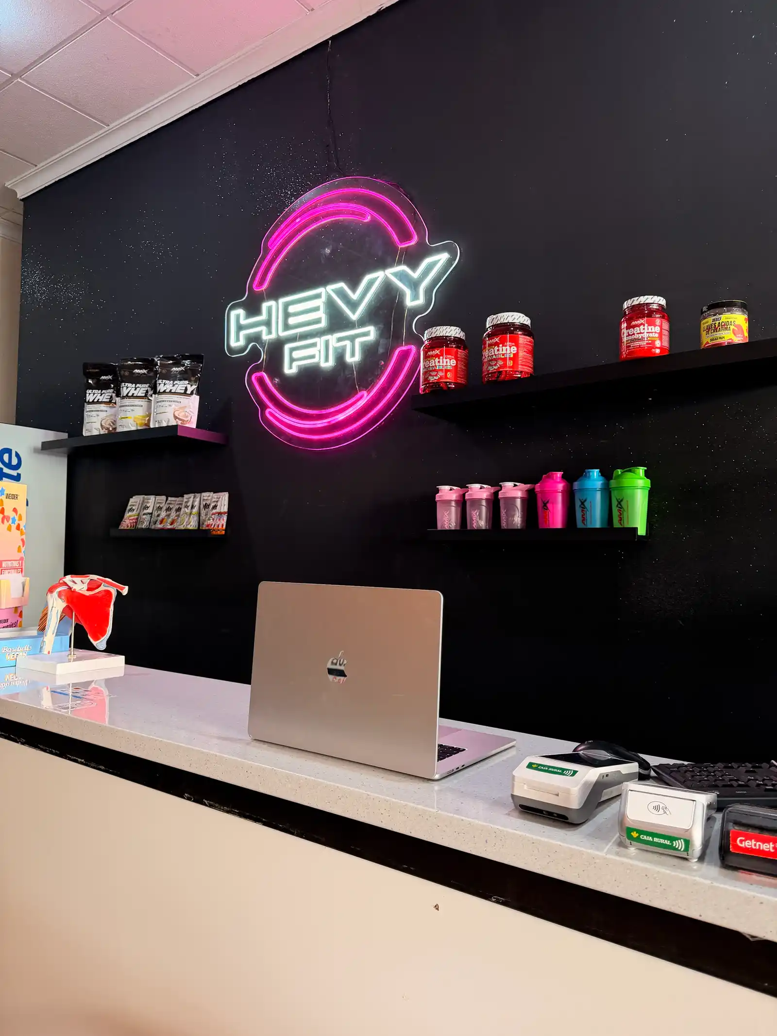 Mostrador de recepción de Hevy Fit con el logo en neón magenta y blanco sobre la pared negra