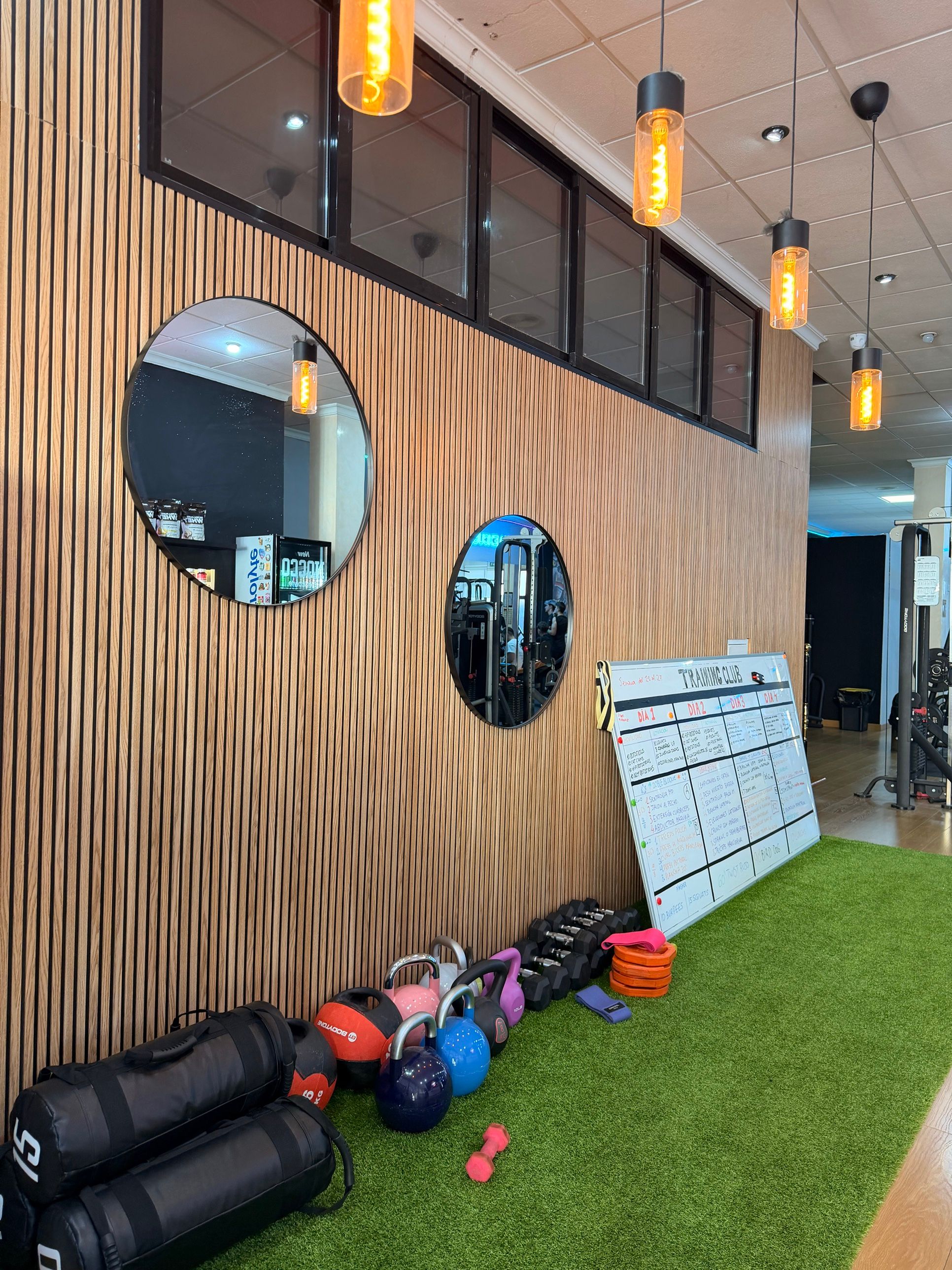 Pizarra del Training Club con la rutina de la semana, kettlebells y sacos sobre el césped